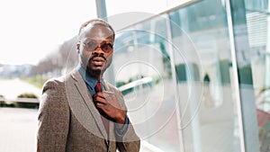 Handsome African American with sunglasses businesman poses in moder suit on the street before a glass building. The