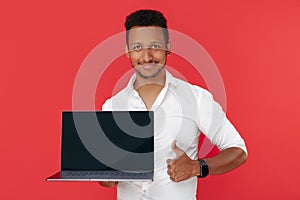 Handsome african american young man holding laptop and show thumb up over red background.