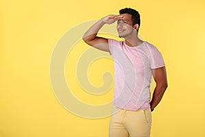 Handsome african american young man looking far away over yellow background.