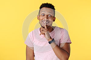 Handsome african american young man show keep silent gesture over yellow background.