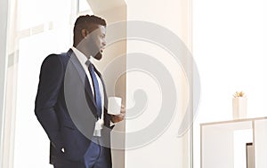 Handsome african businessman drinking coffee near window in office