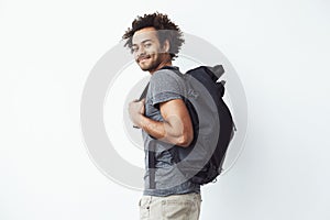 Handsome african man with backpack smiling standing in profile. White background.