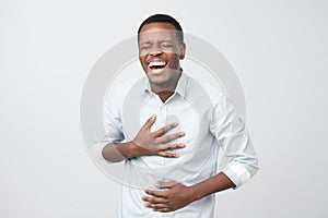 Handsome african man laughing out loud at funny meme or joke he found on internet, smiling broadly.