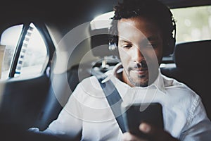 Handsome african man listening music on smartphone while sitting on backseat in taxi car.Concept of happy young people