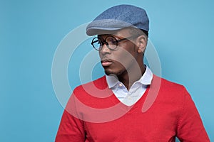 Handsome african young man in blue cao and glasses thinking looking aside