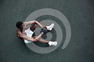 Handsome afro American sportman sitting on the street while taking break after training. Black male having rest after