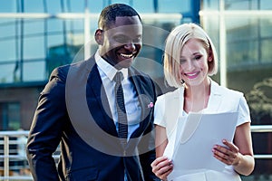 Handsome Afro businessman in a stylish black suit with attractive blonde business lady holding papers and documents of