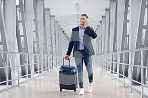 Handsome Arab Man Walking With Suitcase In Airport And Talking On Cellphone