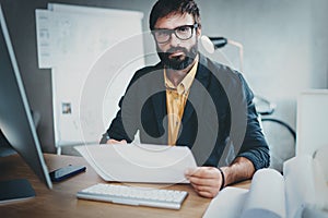 Handsome architect working at sunny office.Bearded young man holding document and looking at the camera.Horizontal