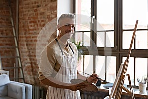 Handsome artist painting a pictures on canvas pose in workshop