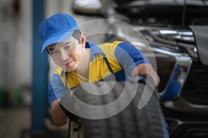 Handsome asian auto mechanic in uniform is examining a tire while working