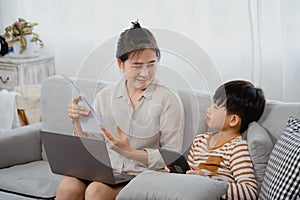 Handsome asian boy and his mother is working on a laptop computer. Frustrated and worried, the little boy pulled the paper from