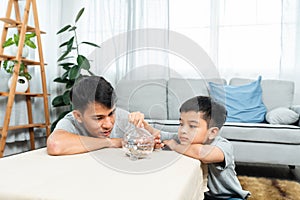 Handsome Asian boy wearing, sitting on floor in front him was table, where piggy bank was placed, boy took coin