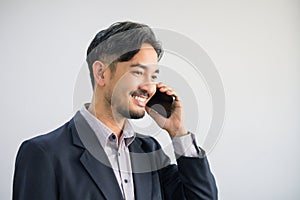 Handsome Asian business man in suit standing and talking on mobile phone, smiling expression showing happiness