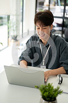 A handsome Asian businessman working on his work on a laptop at his desk in a modern office