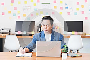 Handsome asian businessman working with laptop in the modern office,typing on laptop and writing down ideas in a notebook.Busy