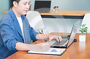 Handsome asian businessman working with laptop in the modern office,typing on laptop and writing down ideas in a notebook.Busy