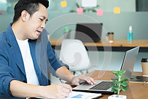 Handsome asian businessman working with laptop in office,watching  on laptop holding call talking on the phone with clients