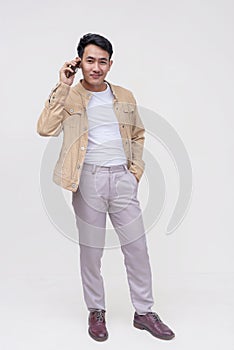 A handsome asian dude in a khaki jacket, white shirt and light gray pants. Holding a phone talking to someone. Whole body photo,