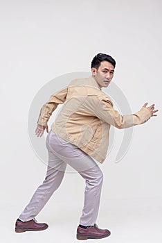 A handsome asian dude in a khaki jacket, white shirt and light gray pants. Making an escape, running pose. Whole body photo,