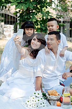 Handsome asian family in white clothes taking selfie in a park, having a picninc