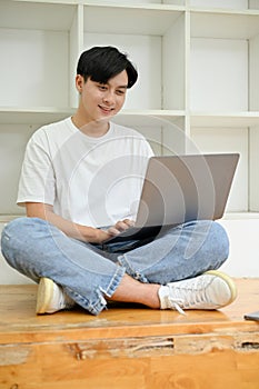 Handsome Asian male college student in library co-working space, using laptop