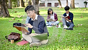 Handsome Asian male college student reading a book and doing homework in the campus`s park