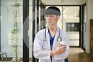 A handsome Asian male doctor in a uniform with a stethoscope stands in the hospital corridor