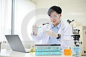 Handsome Asian male scientist adjusts a virus sample in a Petri dish in his science lab