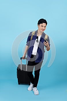 Handsome Asian male tourist wear casual clothes hold suitcase mobile cell phone isolated on pastel blue color background
