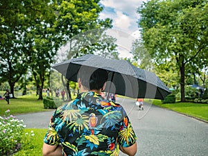 Handsome Asian male wear hawai t -shirt Holding umbrella and walking in the Chatuchak park