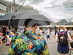 Handsome Asian male wear hawai t -shirt Holding umbrella and walking in the Chatuchak park