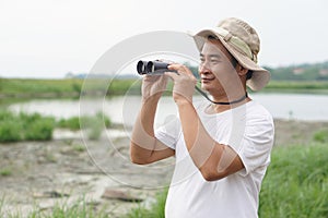 Handsome Asian man ecologist is surveying nature at the lake, holds binoculars. photo