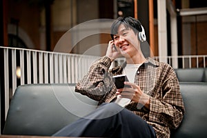 Handsome Asian man enjoys listening to music through his headphones while relaxing in the cafe