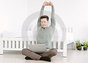 Handsome Asian man freelancer sitting relaxed stretching arms on the floor while working with laptop computer finish work. Korean