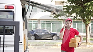 Handsome Asian man holding a cardboard parcel box standing in front of a house with a van in the background, delivery concept.