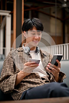 Handsome Asian man holding a credit card and his phone. mobile banking, money transferring