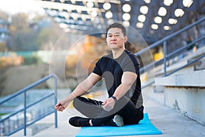 Handsome asian man meditating in modern urban stadium, sitting lotus pose Male practicing yoga mat, zen. relaxes outdoors in