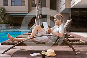 Handsome asian man relaxing by pool and reading e-book