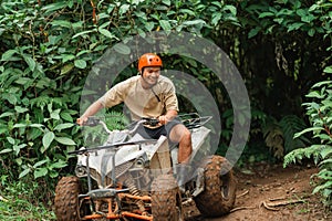 handsome asian man smiling while riding the atv through the difficult terrain