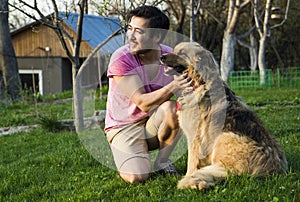 Handsome asian man stroking his fluffy dog on a sunny day in a garden.