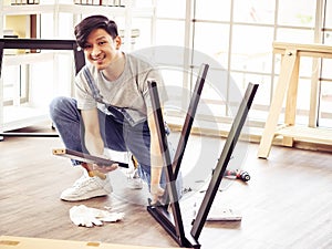 Handsome Asian man trying to assemble knock down furniture , smiling and looking at camera