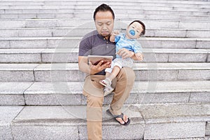 Handsome asian man watching a mobile device with his crying baby