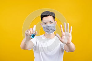 Handsome asian man wearing mask showing hand sanitizer alcohol spray for cleaning stop gesture