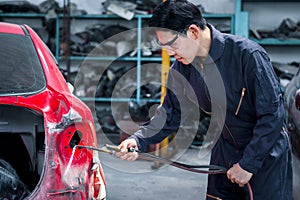 Handsome Asian mechanic man in uniform welding car body panel vehicle, auto mechanic technician fixing, repairing maintenance