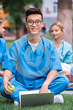 handsome asian medical student holding apple with laptop and looking