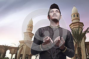 Handsome asian muslim man holding prayer beads and praying
