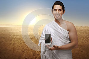 Handsome asian muslim man with ihram clothes showing phone