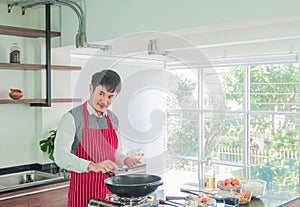 Handsome, Asian young man in Red apron. Cooking for food in the kitchen Room at Home.
