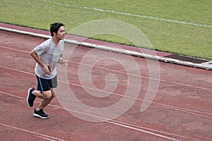 Handsome athlete Asian man running on racetrack in stadium with copy space background. Healthy active lifestyle concept.